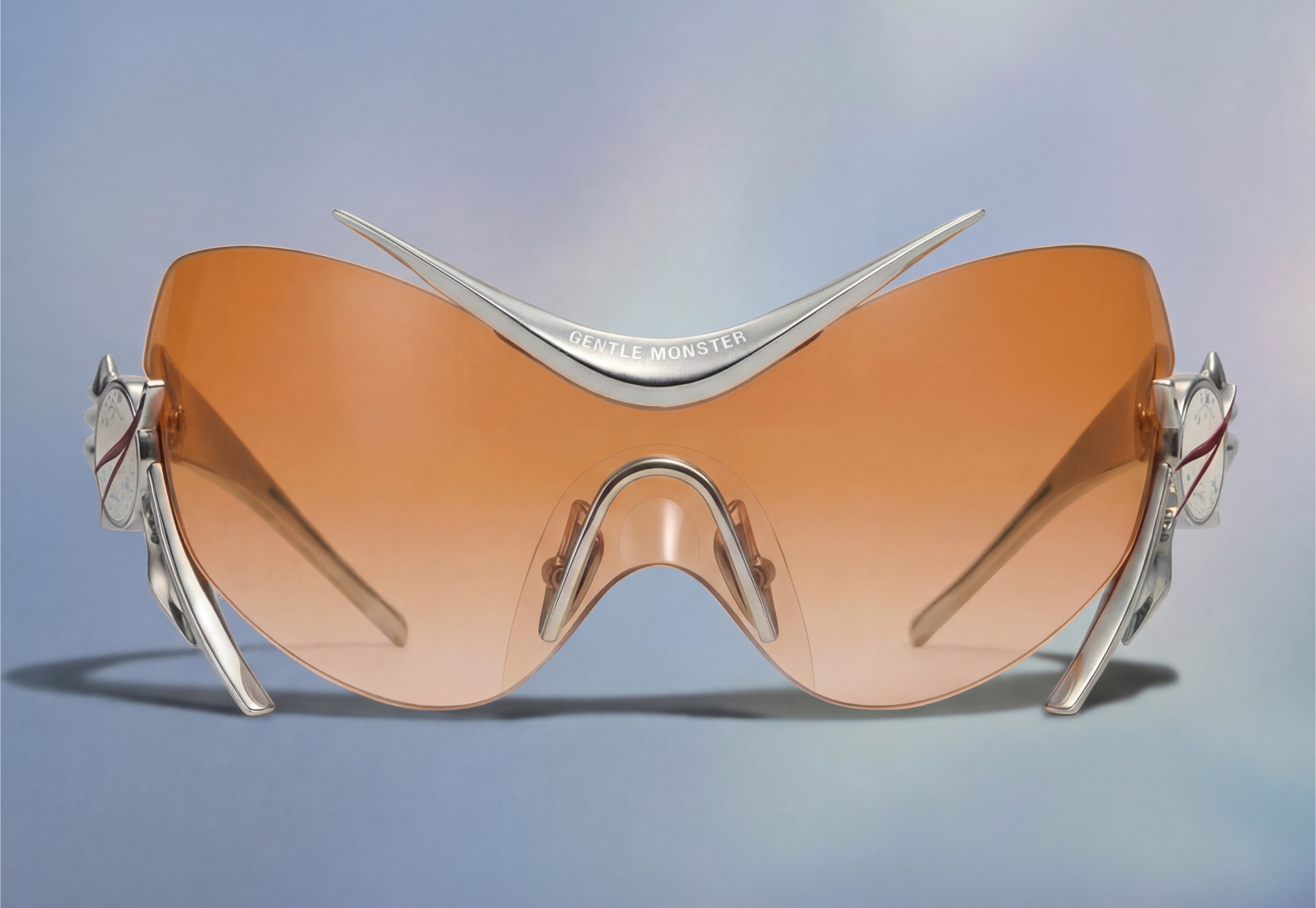 Gentle Moonster, orange-lens glasses against a pale sky-blue ground