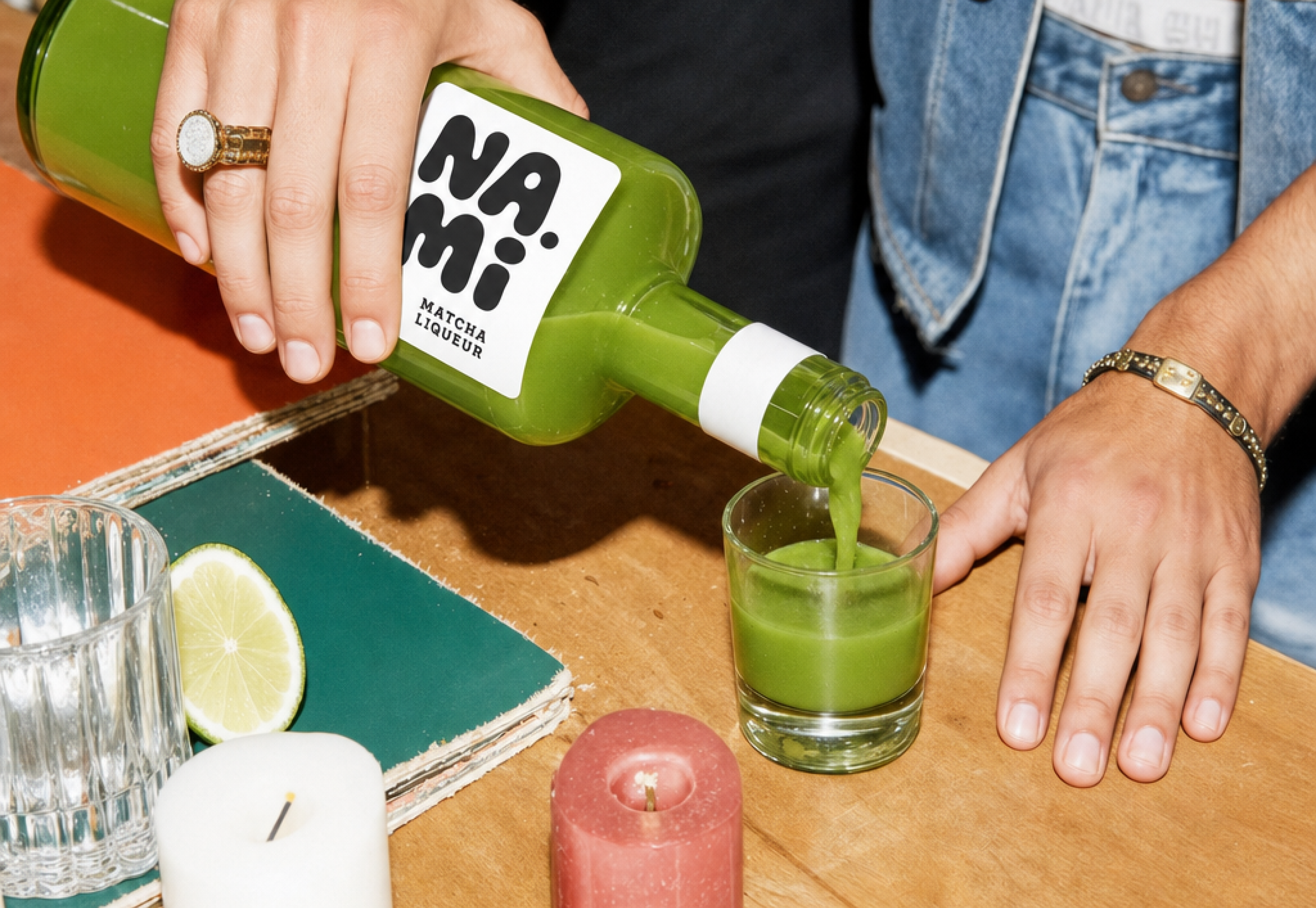 NAMI, a hand pouring the liqueur into a glass on a table